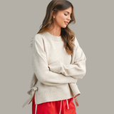 Woman wearing a beige sweater with a tie detail on a gray background