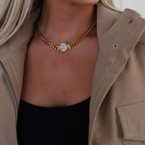 Person wearing a gold chain necklace with a circular pendant, partially visible in a beige jacket.