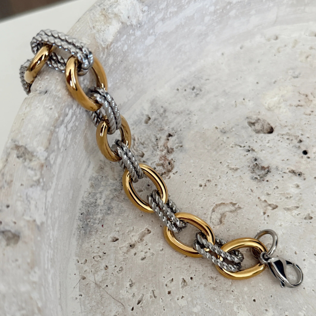 Gold and silver chain bracelet on a textured stone surface
