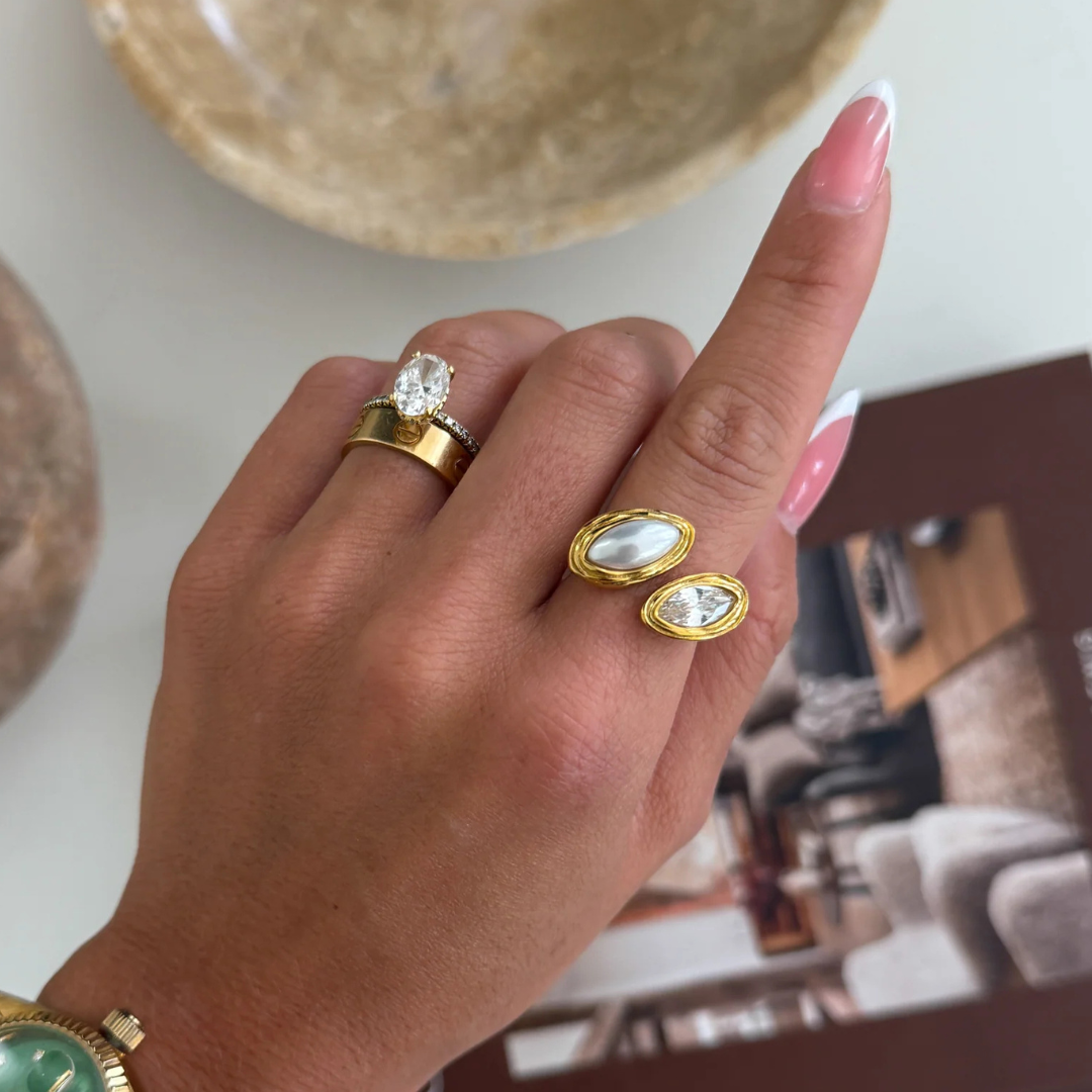 Hand wearing gold rings with gemstones on a blurred indoor background