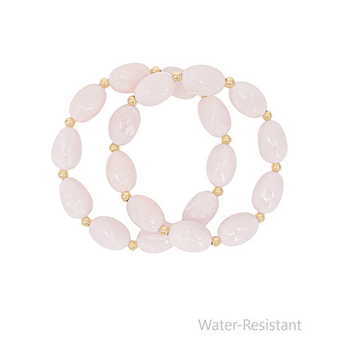 Pink beaded bracelet with gold accents on a white background