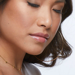 Close-up of a woman wearing a gold hoop earring and necklace on a white background