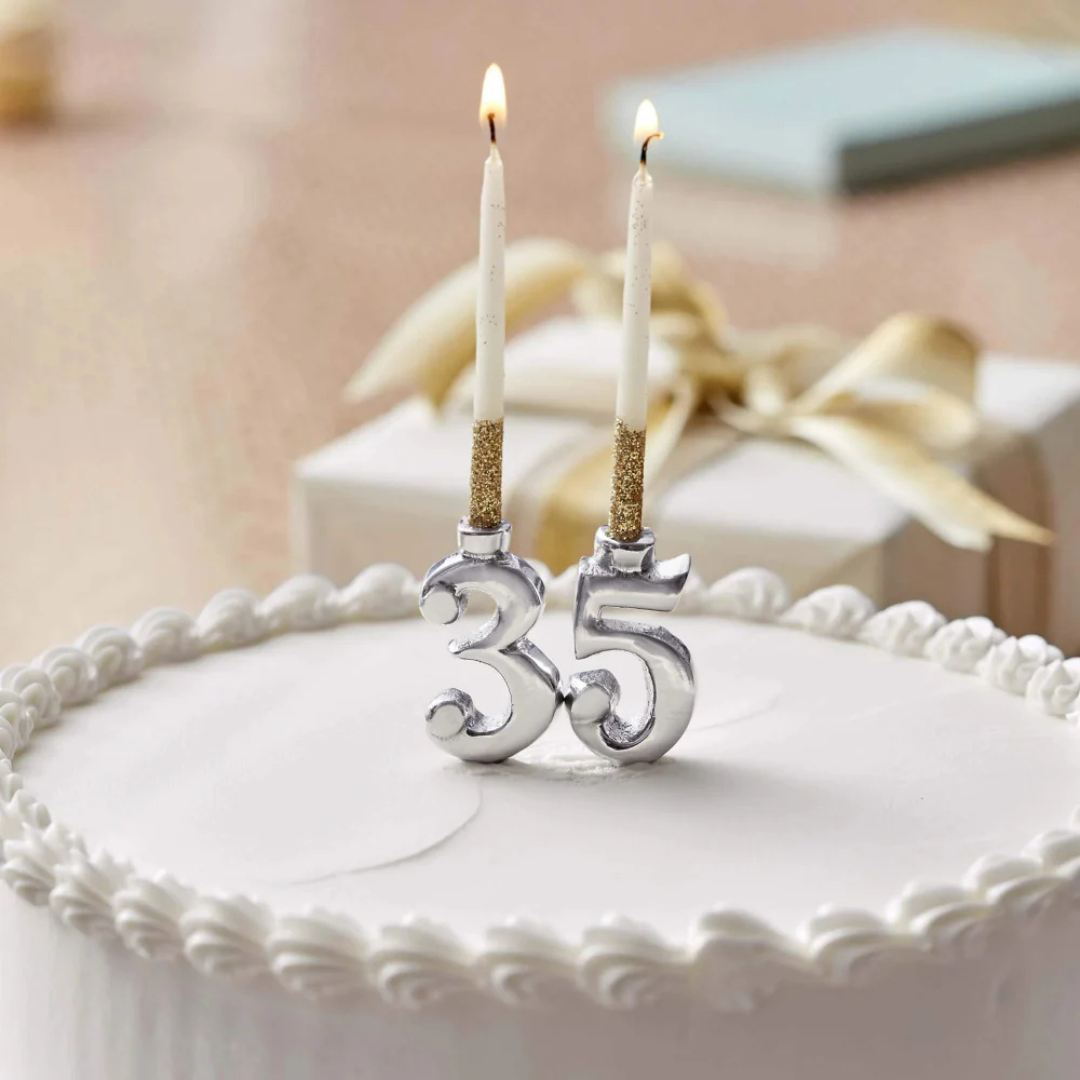 Two lit candles on a cake with decorative numbers '35' against a blurred background.