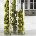 Three tall glass vases filled with green apples on a white surface.
