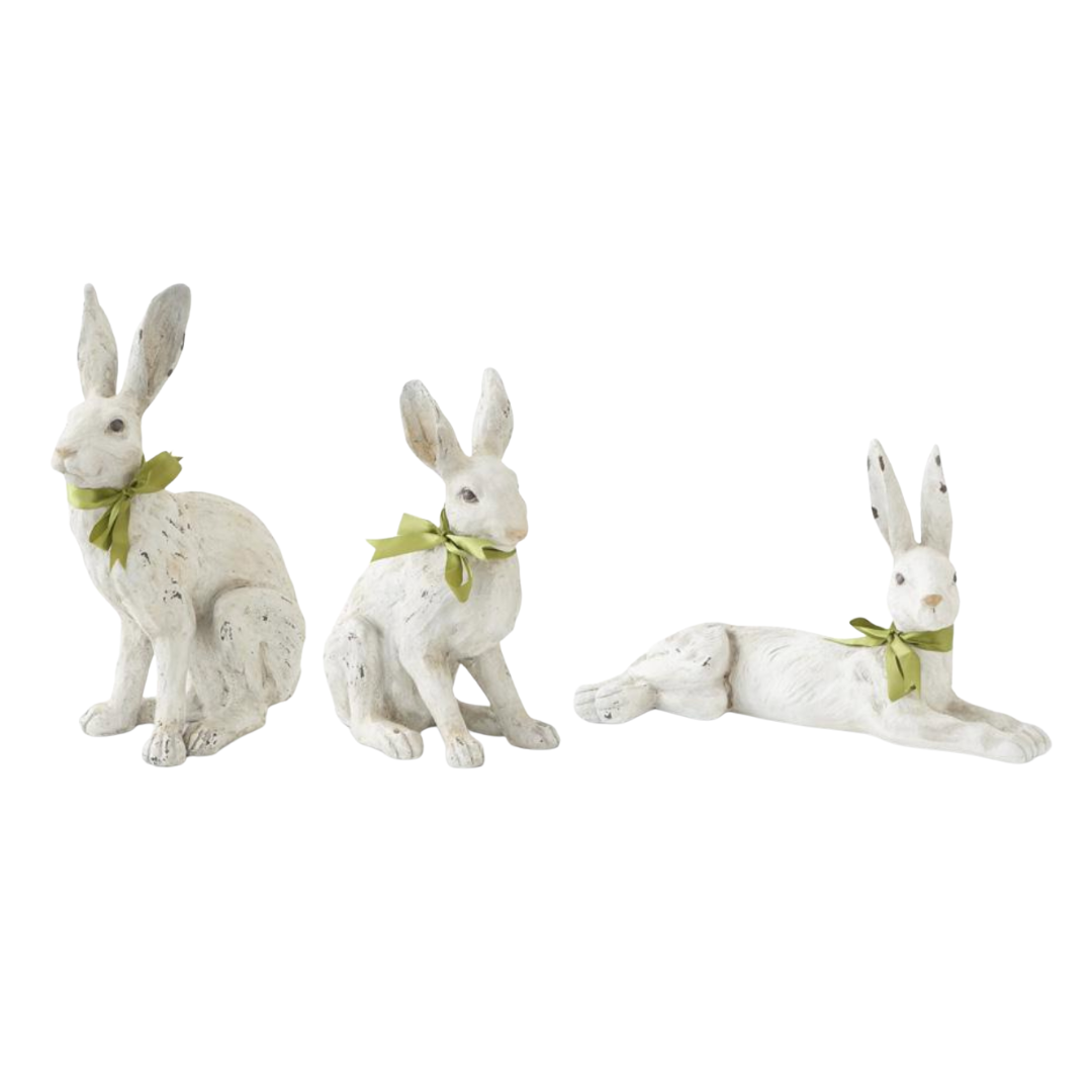 Three white rabbit figurines with green bows on a white background