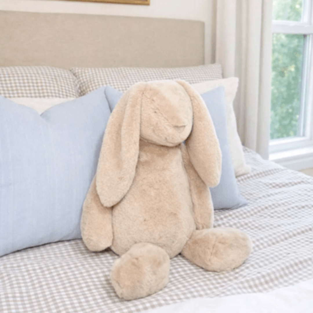 Beige plush bunny toy on a bed with blue pillows