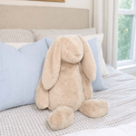 Beige plush bunny toy on a bed with blue pillows