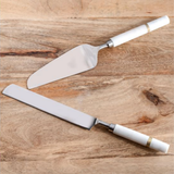 Two cake knives with white handles on a wooden surface