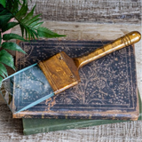 Vintage-style gold paint brush on an old book with a plant in the background