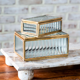 Two stacked glass boxes with gold accents on a marble surface.