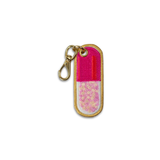 An embroidered pill-shaped keychain charm with a gold-tone metal clasp. The design features a bright pink top half, a red center stripe, and a glittery pink and gold bottom half, all outlined in gold embroidery.