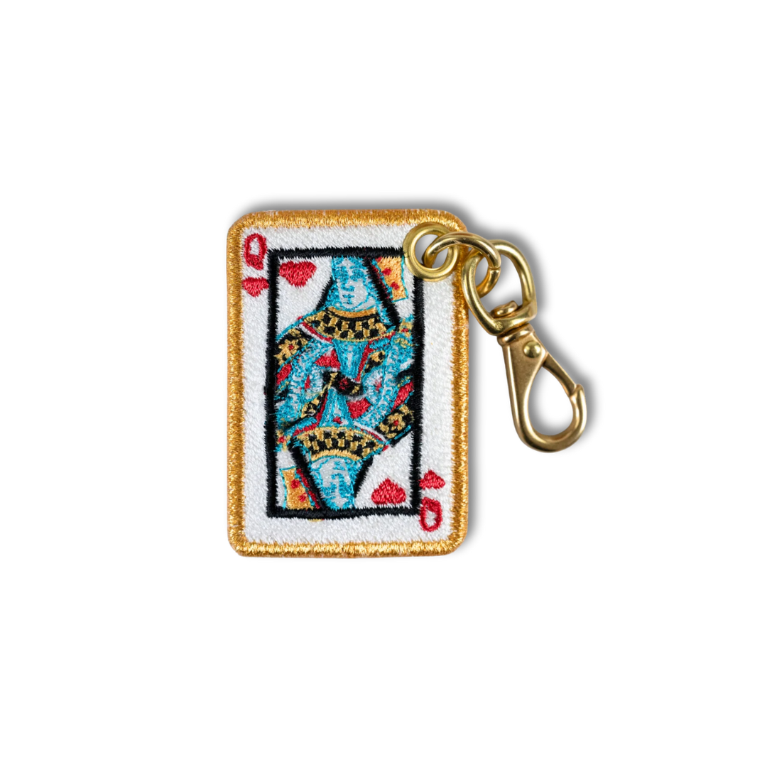 An embroidered keychain charm of a playing card queen with a gold border and a gold metal clasp, shown on a plain white background.