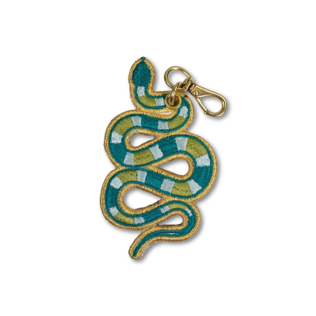 A snake-shaped embroidered keychain charm with a gold border, featuring green, yellow, and white stripes, complete with a gold lobster clasp at the top, shown on a plain white background.