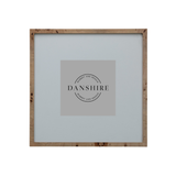 A square picture frame with a natural light brown wood border and a light gray mat, featuring a central gray placeholder card with the brand name 'DANSHIRE' printed in black.