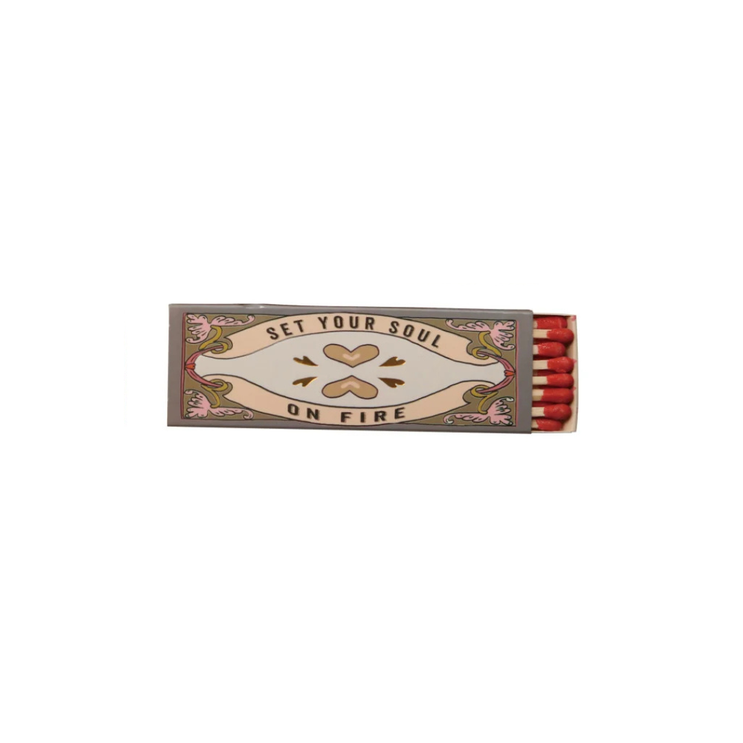 A decorative matchbox with the words 'SET YOUR SOUL ON FIRE' and a heart motif, shown open with red matchsticks visible against a plain white background.