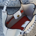 White handbag with black and white striped handles, red interior, and visible brand name.