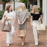 Three women walking outdoors, each holding a handbag, on a brick path.