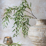 Artificial faux willow stem with cascading green leaves on a natural branch, styled in a large textured ceramic vase for an organic, flowing arrangement.