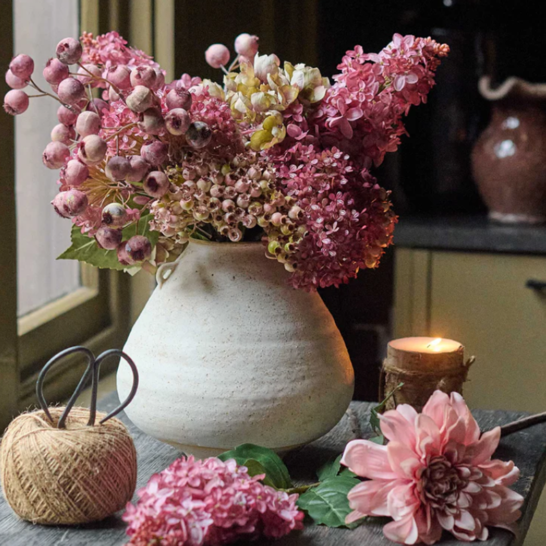 Decorative still life with pink flowers in a white vase on a table.