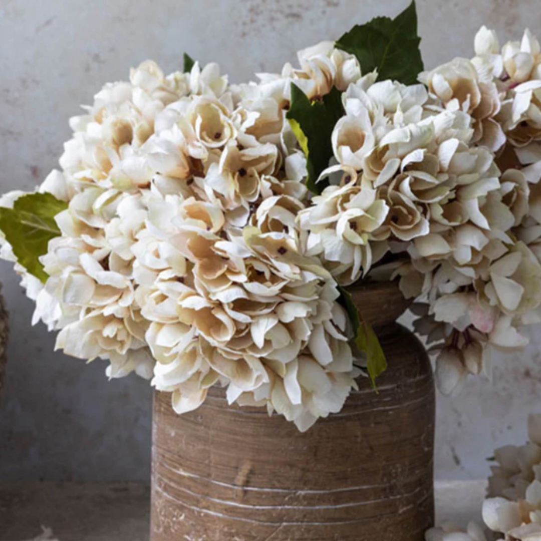 Decorative bouquet of white and beige flowers in a rustic vase against a neutral background