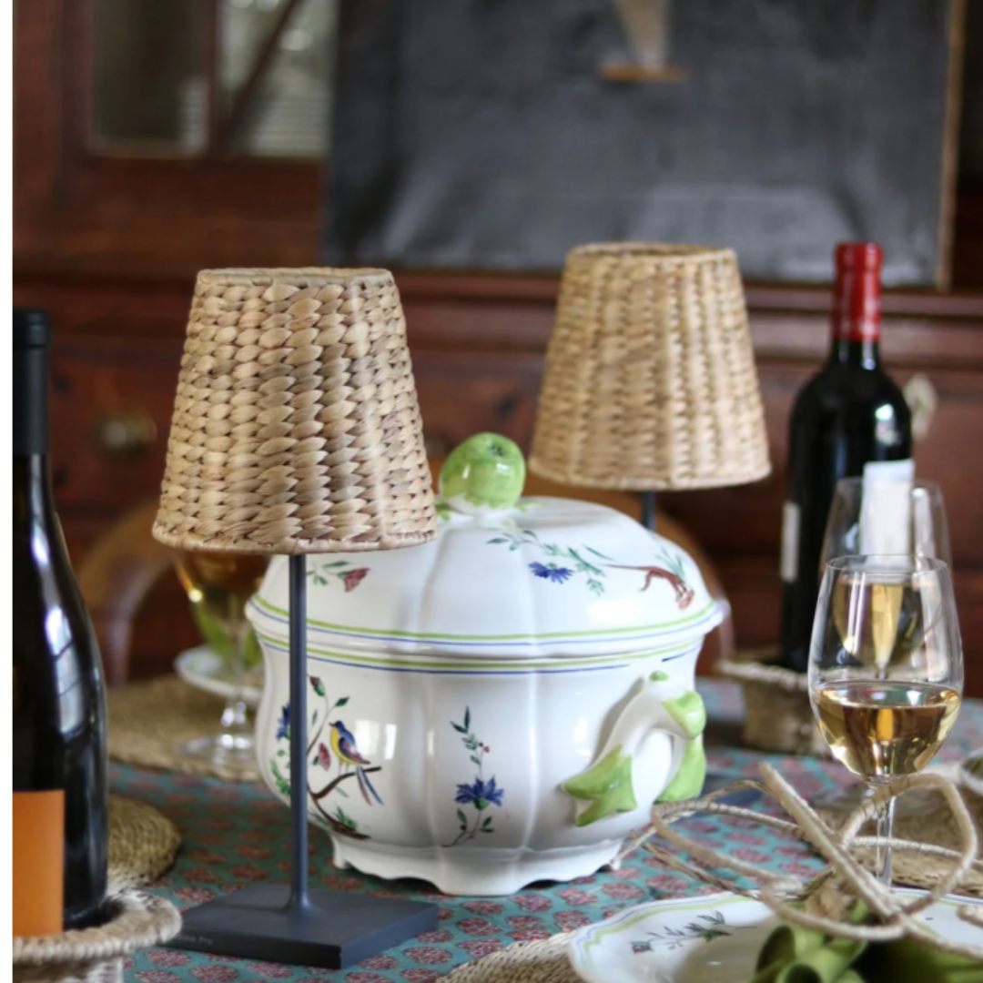 Decorative table setting with a ceramic tureen, lamps, and wine bottles.