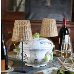 Decorative table setting with a ceramic tureen, lamps, and wine bottles.