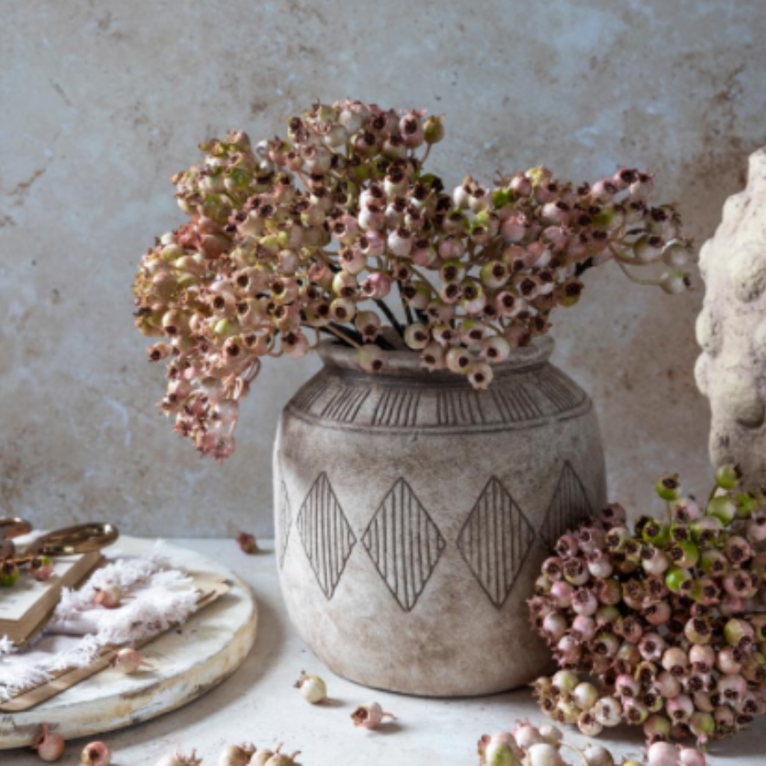 Decorative vase with geometric patterns on a light surface with flowers and a plate.