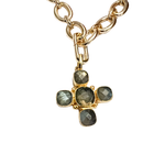 Faceted stone cross charm in gold-tone bezel hanging from a gold link necklace on a white background.