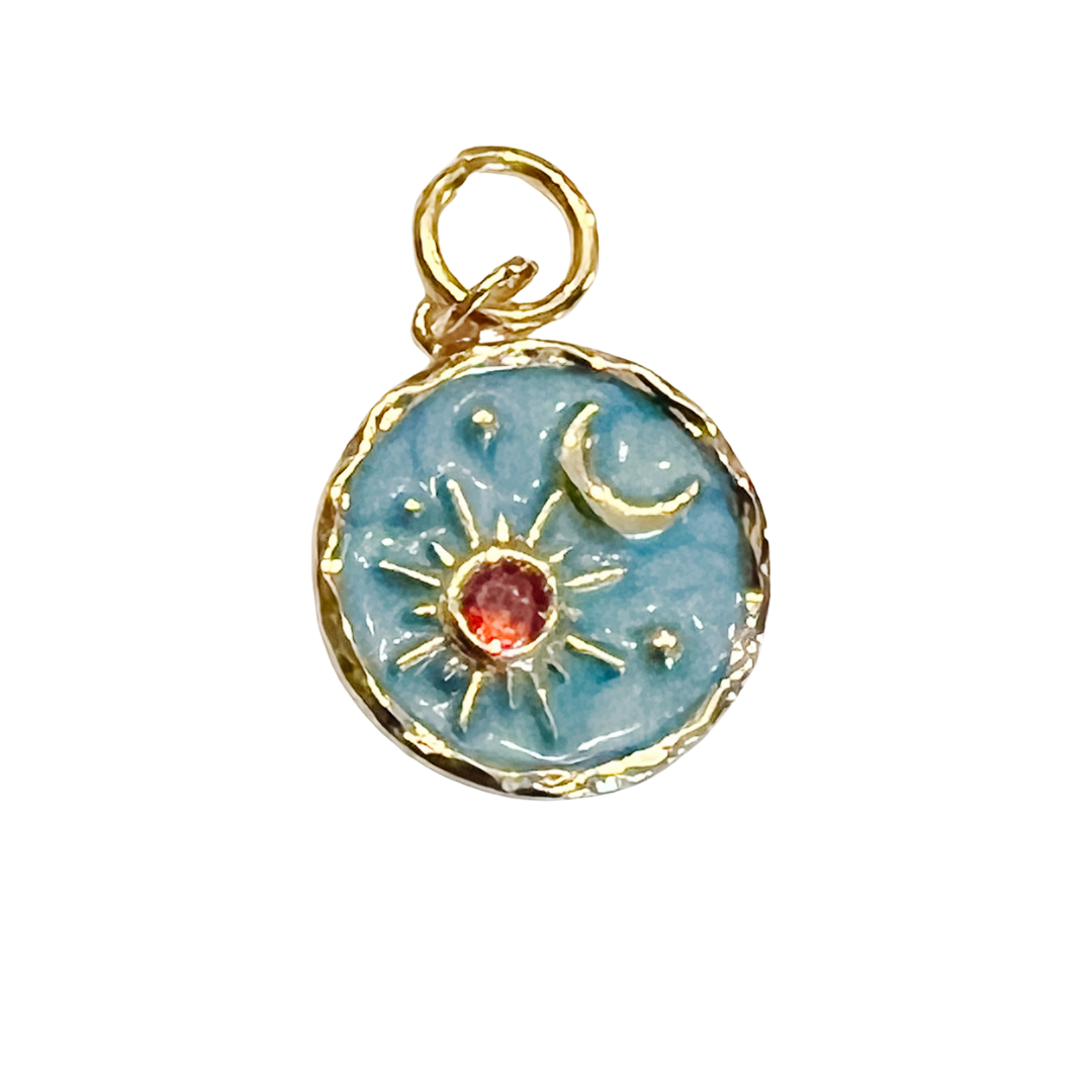 Round blue celestial charm with gold sun, crescent moon, star details, and a small red center stone on a white background.