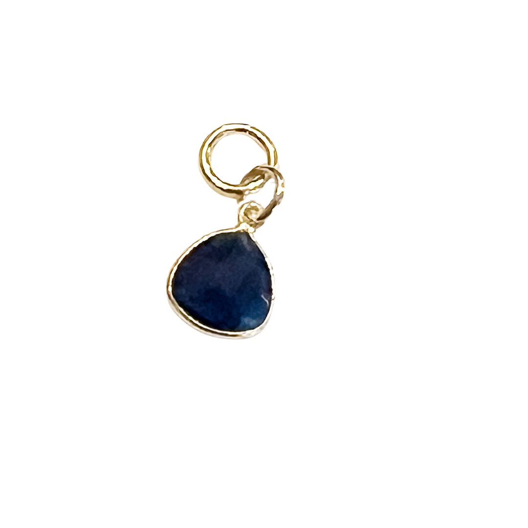 Polished deep blue stone charm with gold bezel and small attachment loop on a white background.