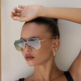 Woman wearing gold sunglasses and hoop earrings with a neutral background