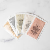 Five skincare sheet masks on a marble surface