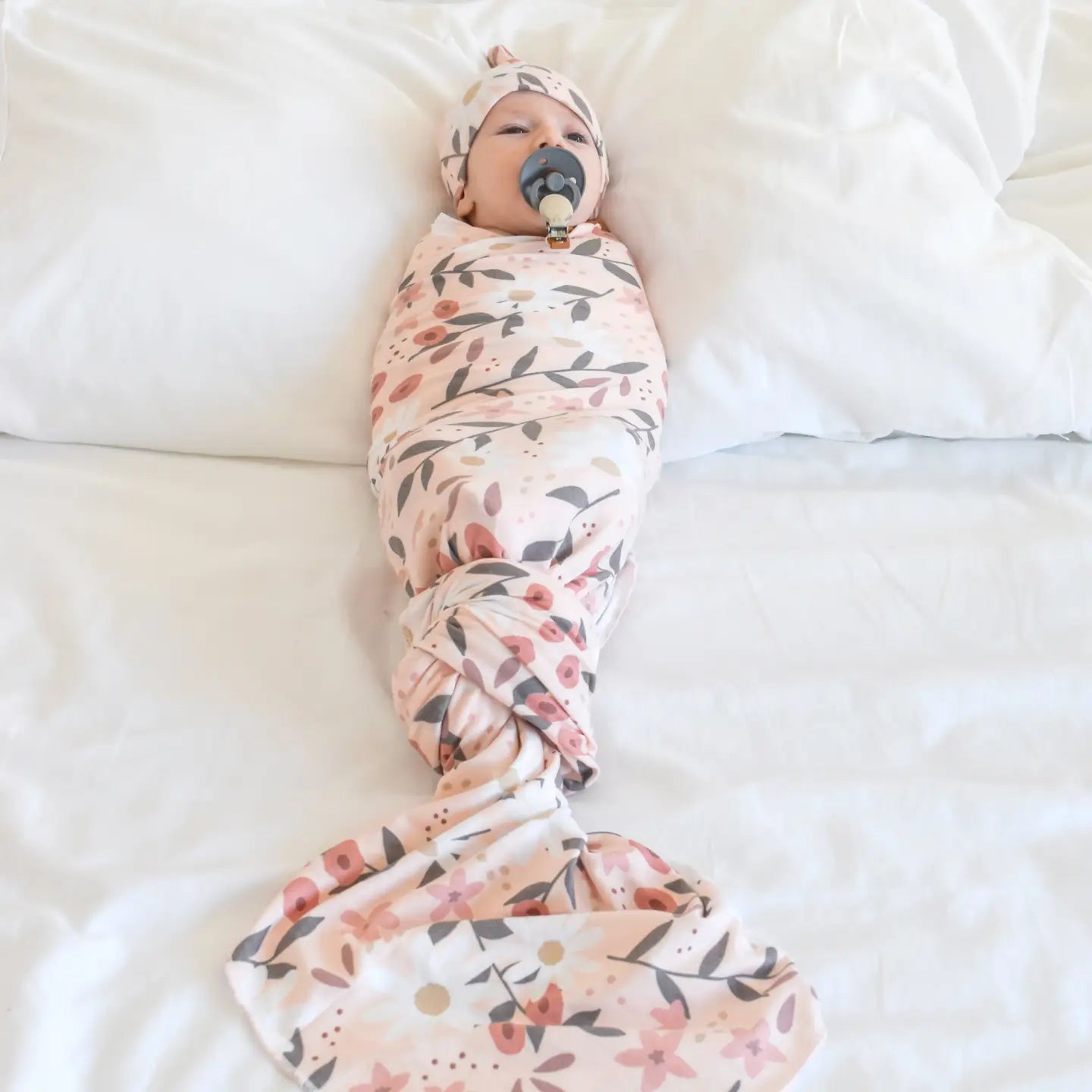 Baby swaddled in a floral blanket on a white surface