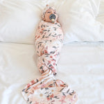 Baby swaddled in a floral blanket on a white surface