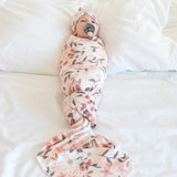 Baby swaddled in a floral blanket on a white surface