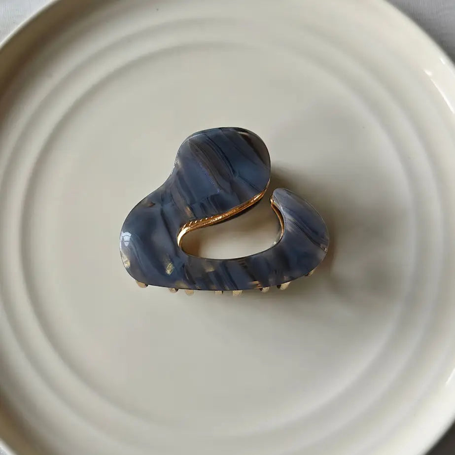 Blue marbled hair claw with gold accents on a white ceramic plate