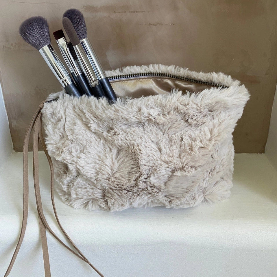 Beige fluffy bag with makeup brushes on a marble surface