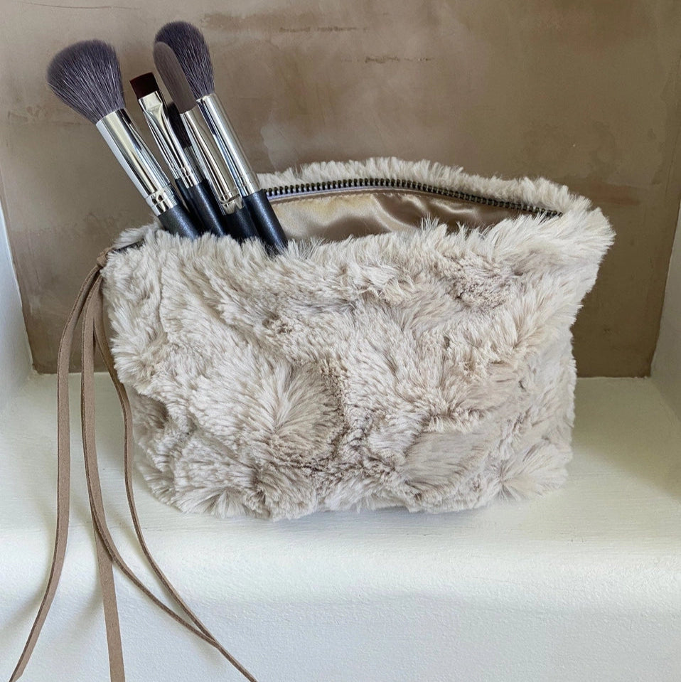 Beige fluffy bag with makeup brushes on a marble surface