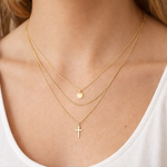 Close-up of a person wearing two gold necklaces with a cross pendant.