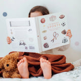 Child reading a book with a teddy bear on a bed