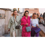 Three women walking together with fashionably styled outfits and handbags in front of the Eiffel Tower.