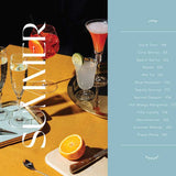 Cocktail menu with various drinks and a smartphone displaying a cocktail app on a wooden table.