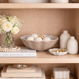 Decorative shelf with a bowl, vase, books, and flowers on a wooden shelf.
