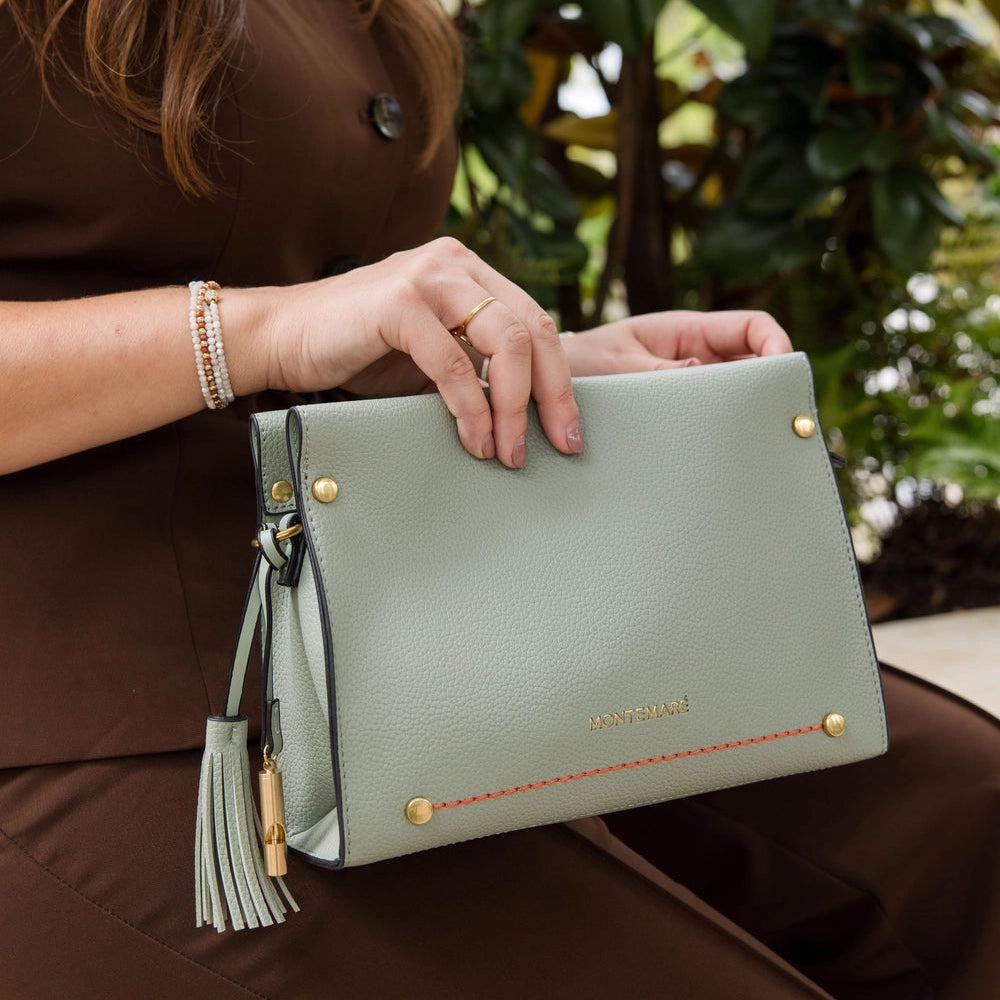 Person holding a Montemare's Vienna Crossbody in Blakes Blue with gold accents against a blurred natural background