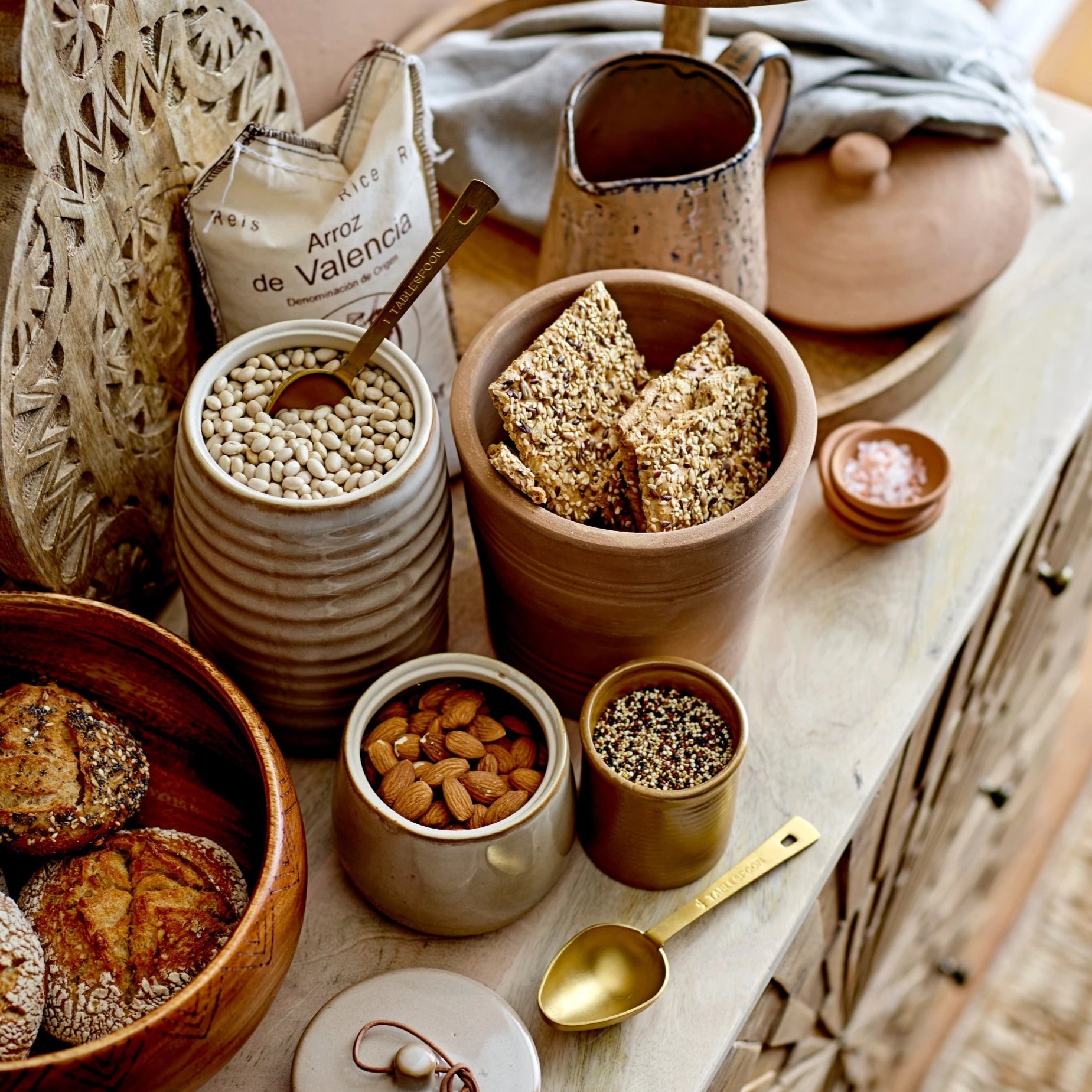 Table setting with ceramic containers, bread, and a pitcher on a wooden surface.