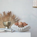 Decorative bowl with textured surface holding coconuts on a white surface with a neutral background