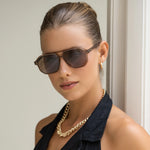 Woman wearing sunglasses and a gold necklace against a neutral background