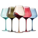 Five wine glasses of different colors with varying levels of red wine on a white background
