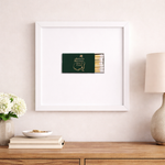 Framed artwork of a matchbox on a wall above a wooden surface with decor items.