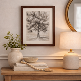 Decorative setup with a vase, books, and lamp on a wooden console table against a wall with framed artwork.